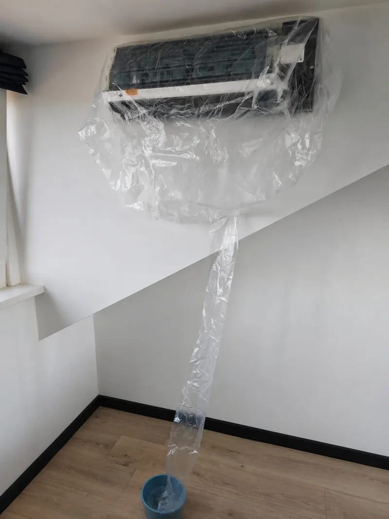 Binnenunit afgedekt met speciale waterzak tijdens schuimreiniging, het vuile water loopt gecontroleerd af in een emmer